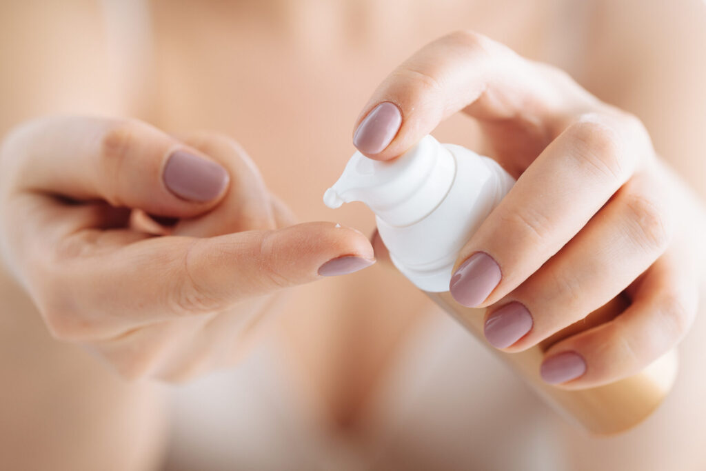 woman hands applying moisturizing cream to her skin using airless pump bottle