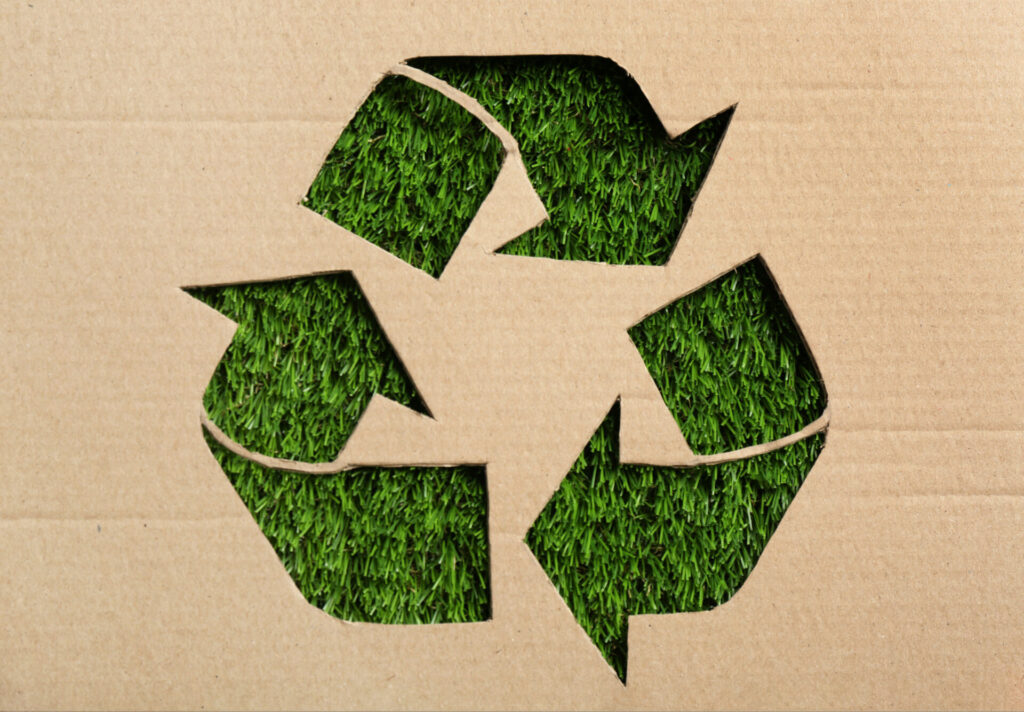 Sheet of cardboard with cutout recycling symbol on green grass
