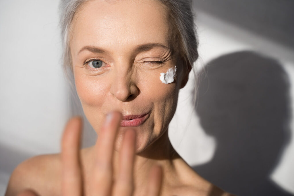 Woman with protective skin care cream and moisturizer lotion from airless pump bottle on her happy smiling face